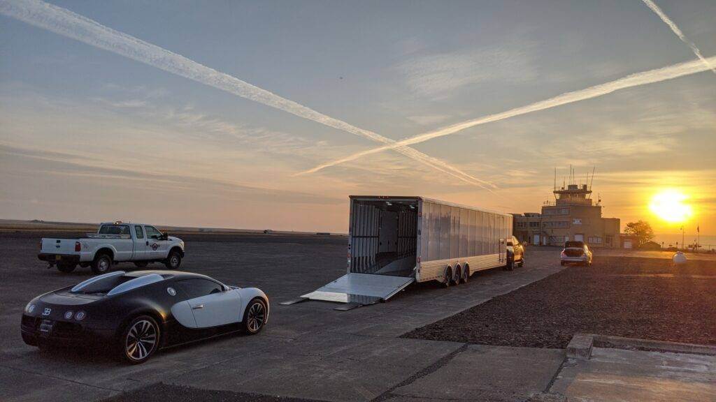 Sun setting just to the right of an air traffic control tower, with a black and white Bugatti loaded onto an enclosed trailer in white. Enclosed car shipping is our expertise. Enclosed car transport is a very common car shipping method for high-end cars.