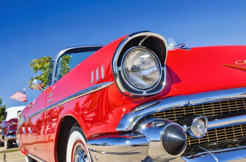 classic car dealership beautiful red Chevrolet Bel-Air convertible on a bright sunny day with the American flag in the background. Classic car dealership near me.