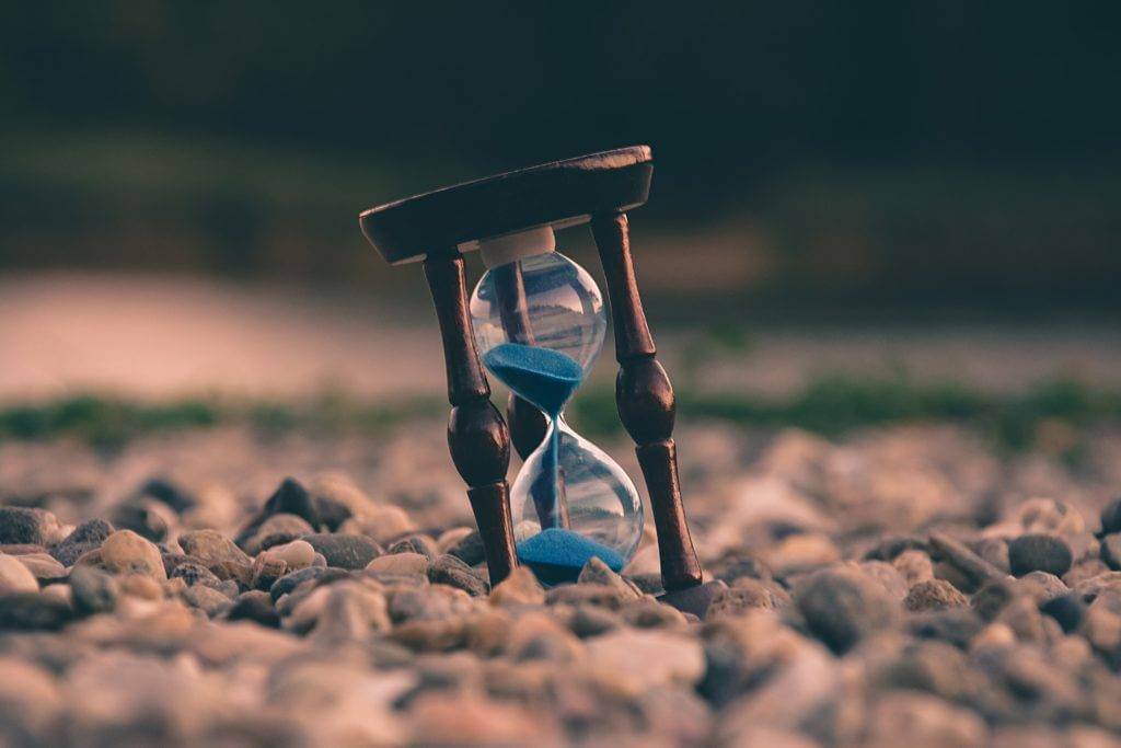 An hour glass standing on small rocks. Car shipping cost.