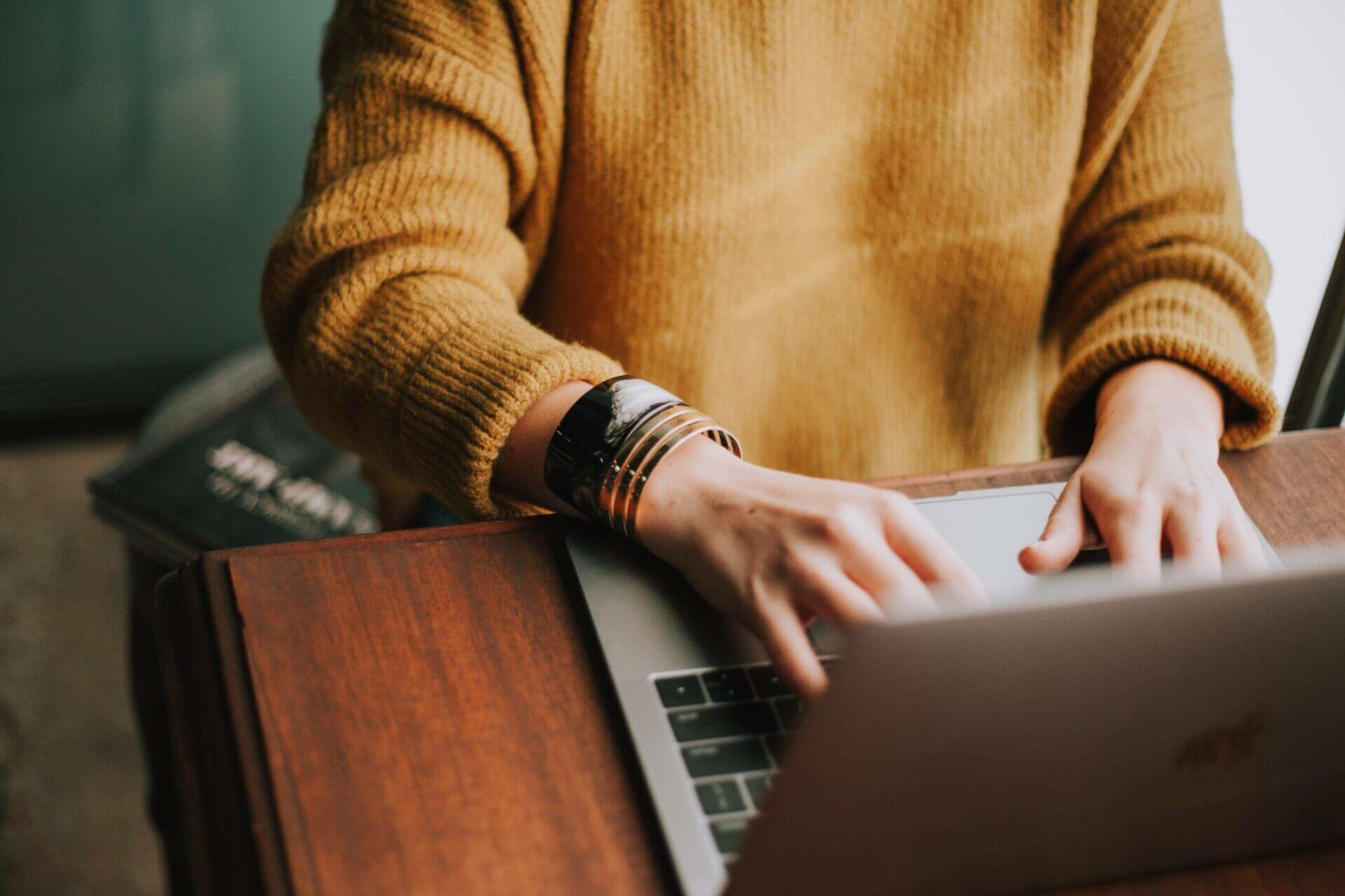 someone wearing a tan sweater searching on their laptop for car shipping quotes.