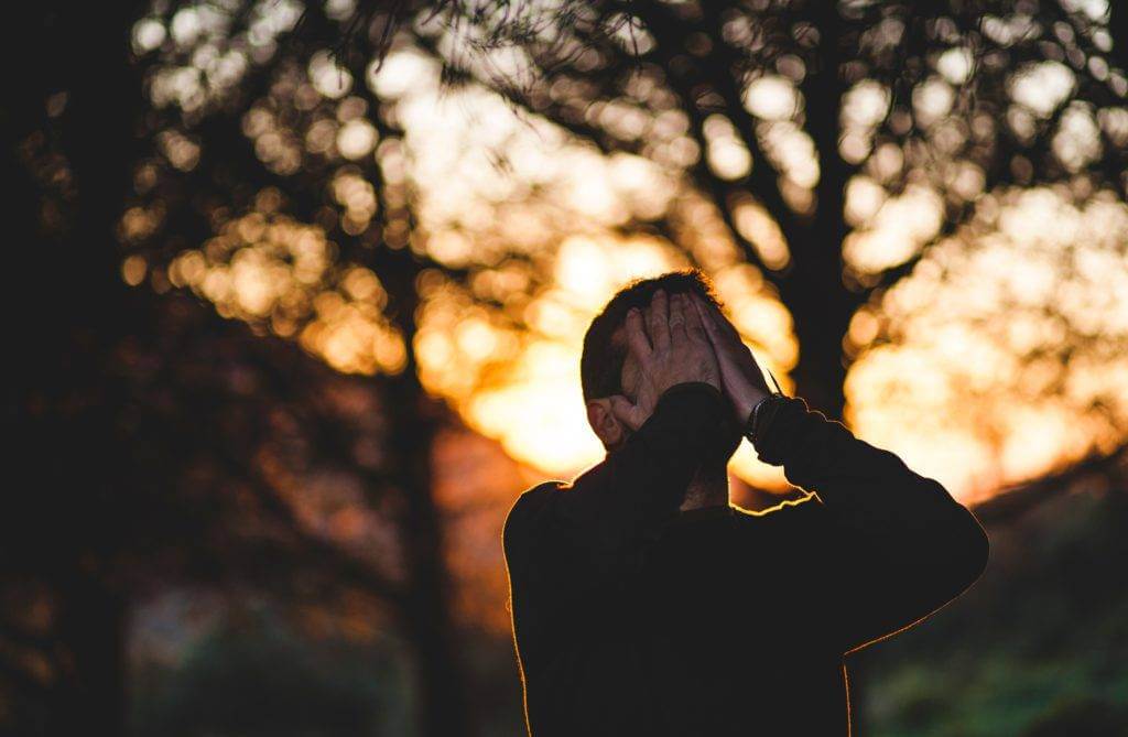 A man with his hands on his face expresses stress. Get free auto transport quotes.