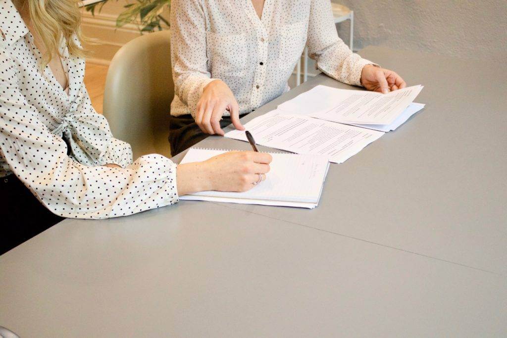 Two women are going through essential documents. They are preparing their paperwork for shipping a car. 