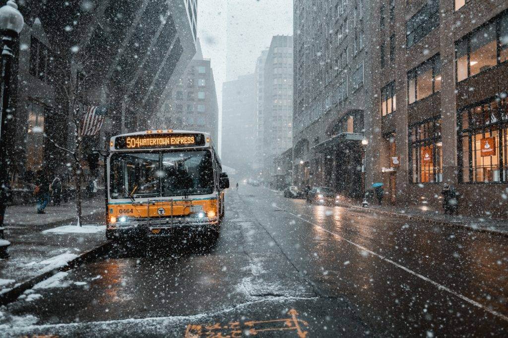 A public bus on a city street with heavy snowfall. Make sure to get enclosed car shipping for added protection from bad weather.