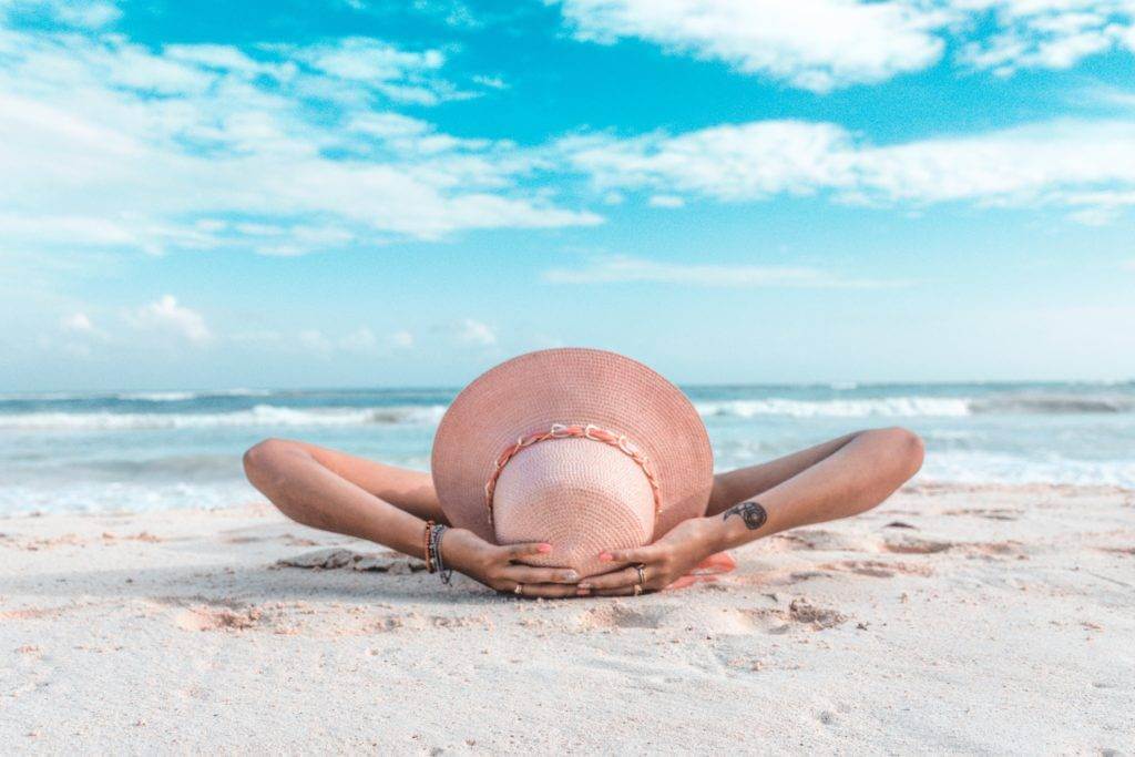 Woman laying down on a sandy beach. Car shipping cost.