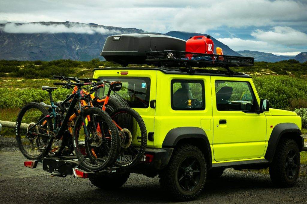 A vehicle with a roof rack packed with luggage and a rear bike rack holding two bikes. Vehicle shipping.