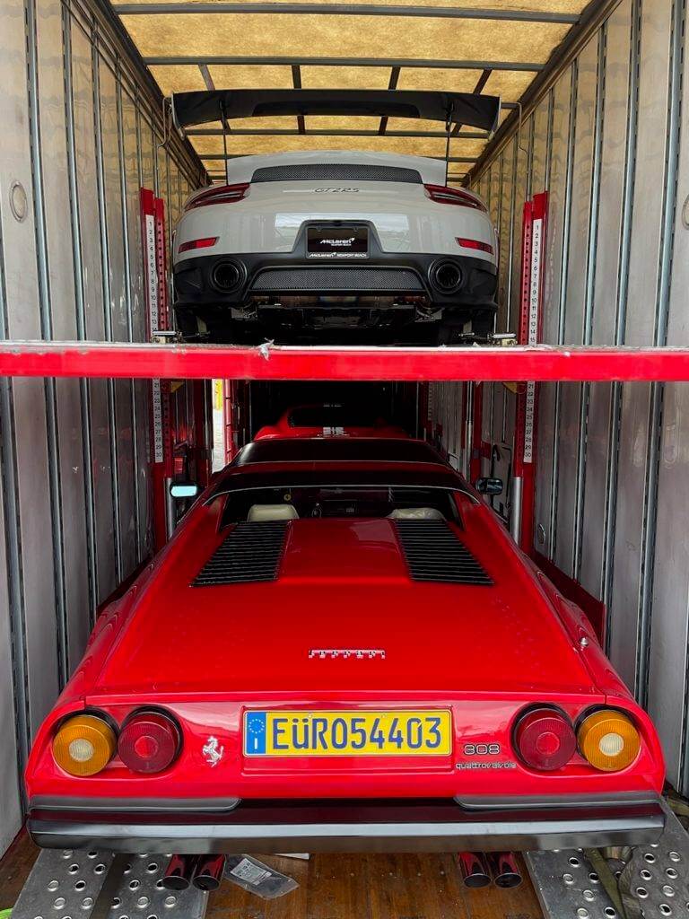 Inside an enclosed trailer. Looking at the rear end of a classic Ferrari and a modern Porsche.