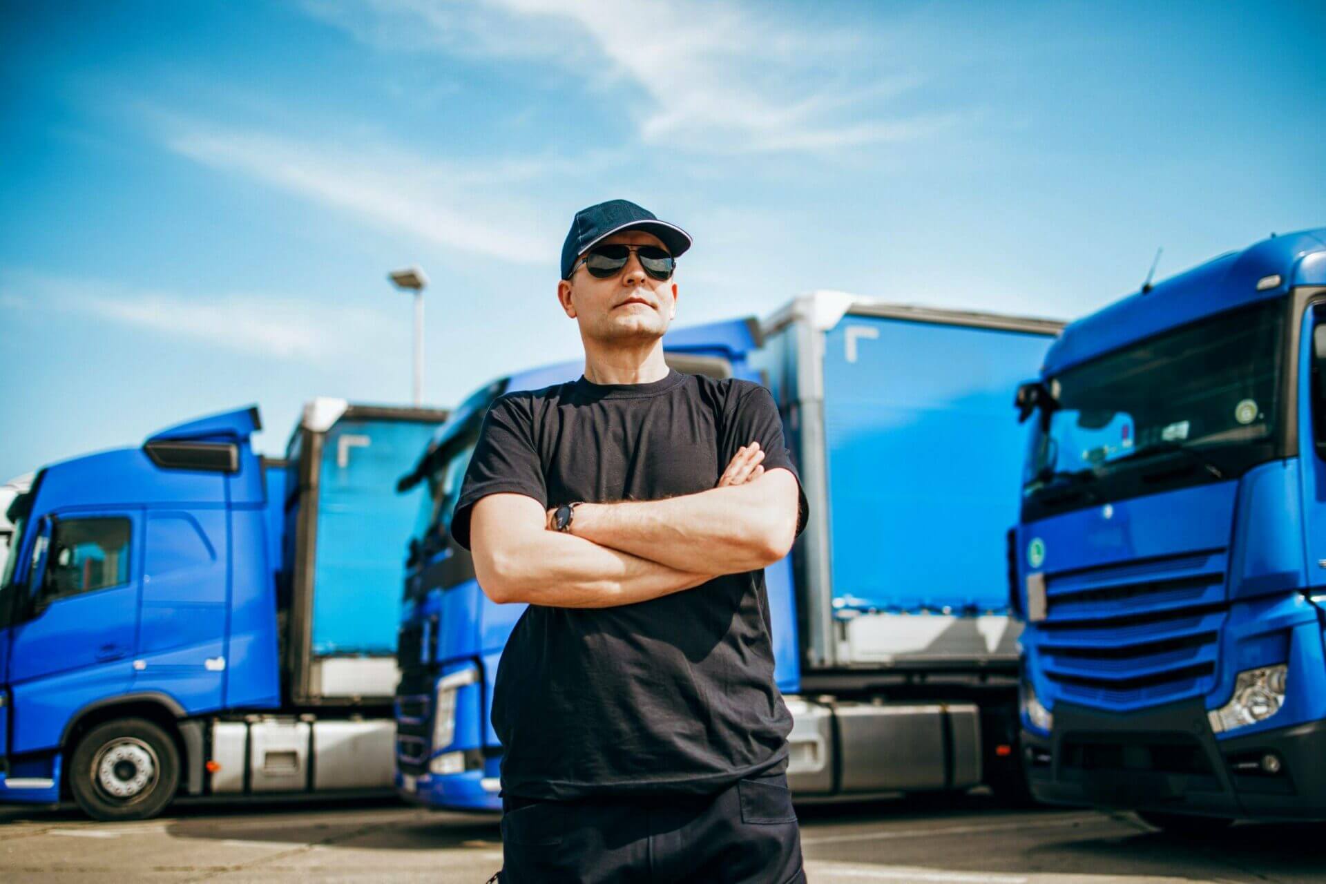 A car carrier driver is standing in front of his truck with his arms crossed. Only the very best car shipping companies vet each and every car carrier.
