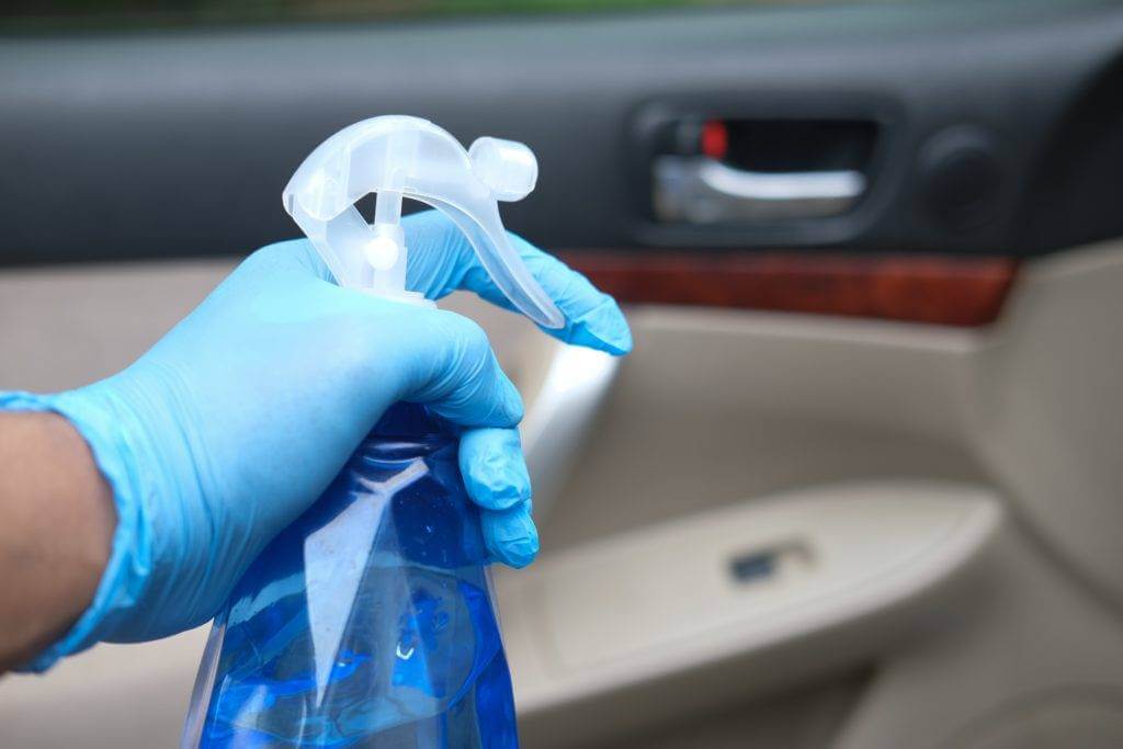 Hand with a blue rubber glove holding a car interior cleaning spray bottle. Whether you need a luxury car or exotic car transport services, make sure to prepare the vehicle before you have the car transport.