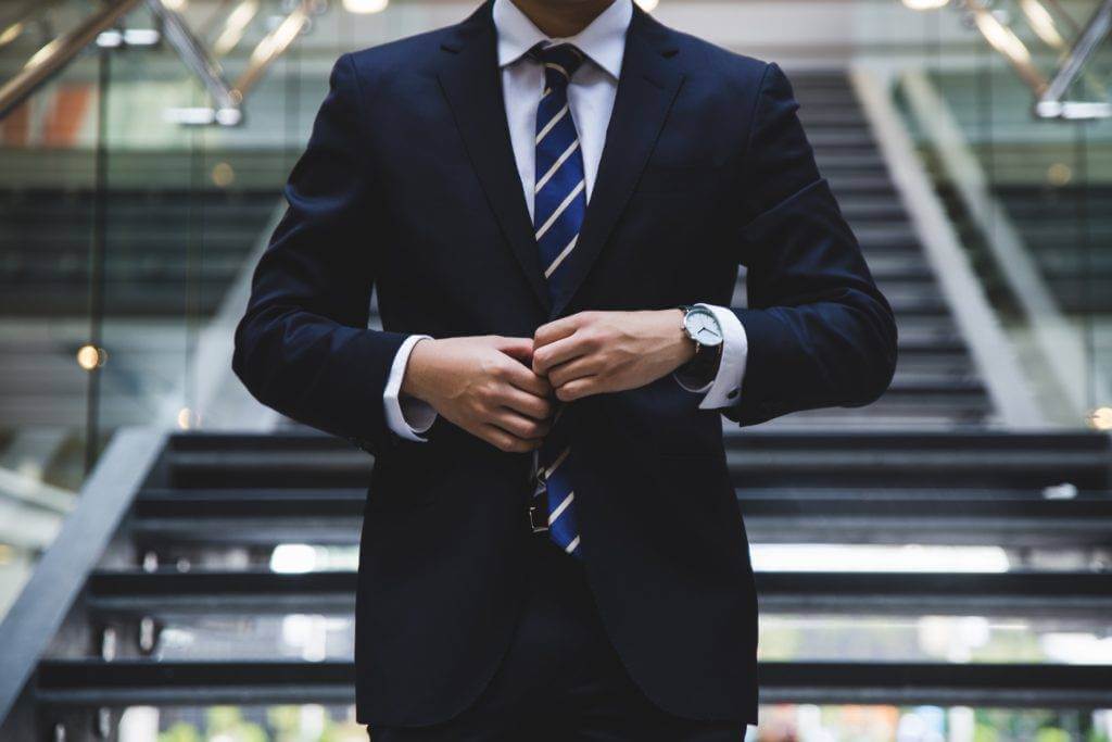 A businessman walks downstairs, adjusting his suit jacket button. New car and used car prices have held their values in the past few years. Instead of falling behind on car payments with a new car, consider opting for a used car that holds its value.